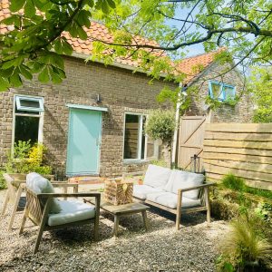 Rustieke achtertuin met zitgedeelte en bakstenen huis.
