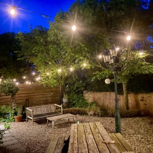 Verlichte achtertuin met houten meubels en bomen.
